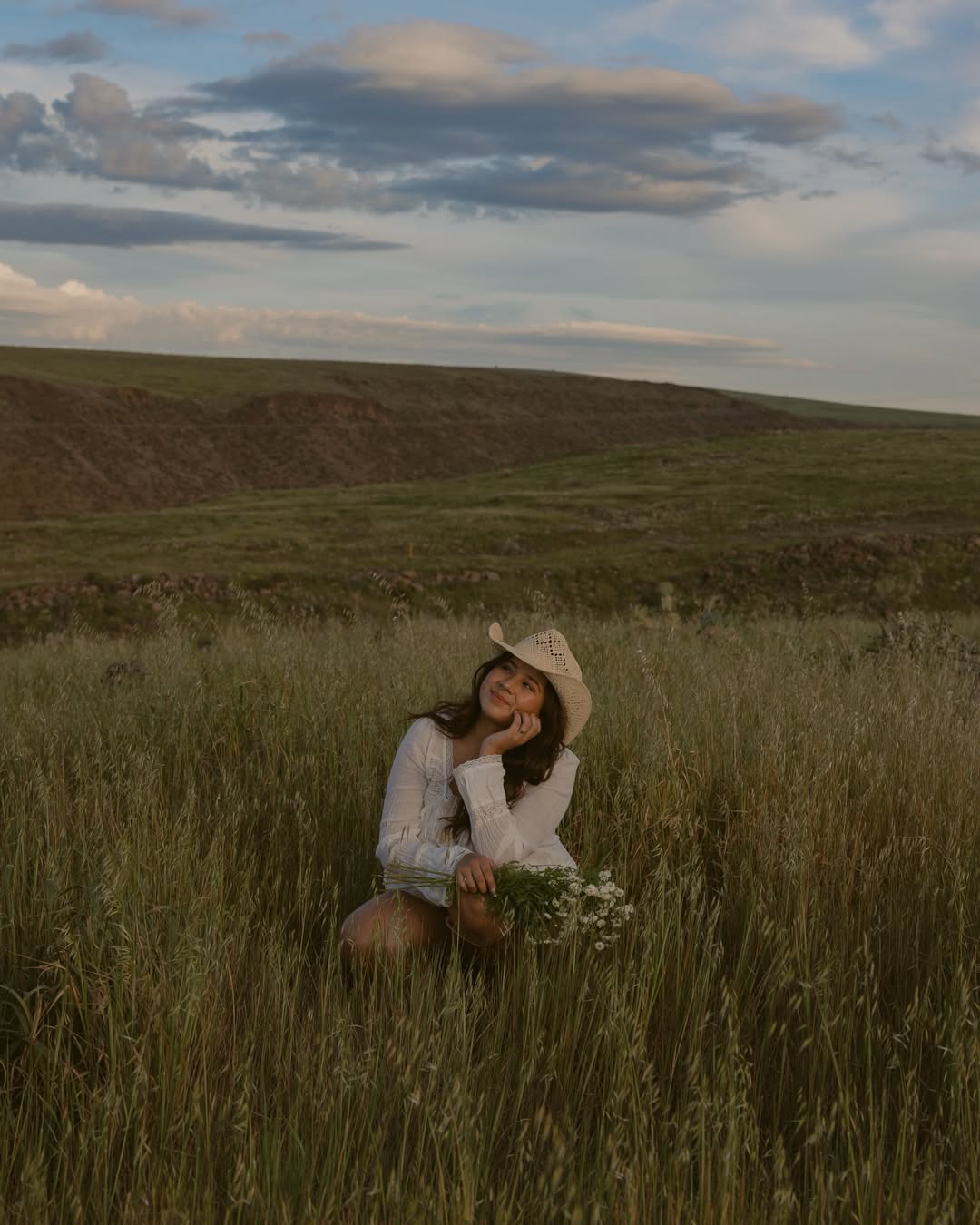 Mars, Arizona photographer sitting in a sunlit grass field wearing a white dress and cowboy hat